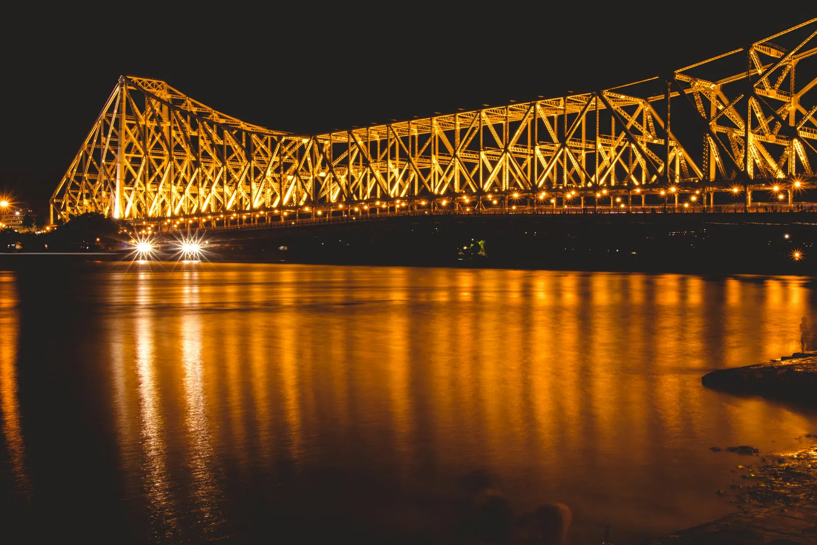 Howrah Bridge illuminated in golden light at night, reflected in the Hooghly River